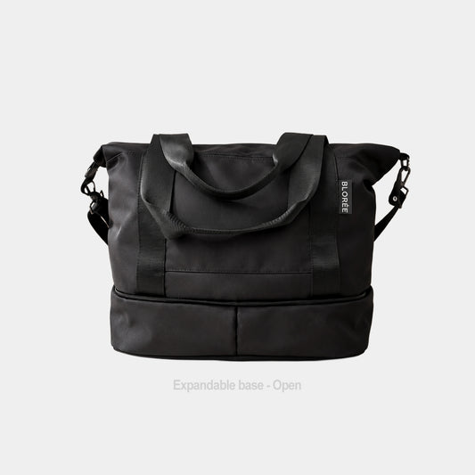 A black expandable duffel bag with dual top handles, a detachable shoulder strap, and a lower zippered compartment, shown on a light gray background with text reading 'Expandable base - Open'.